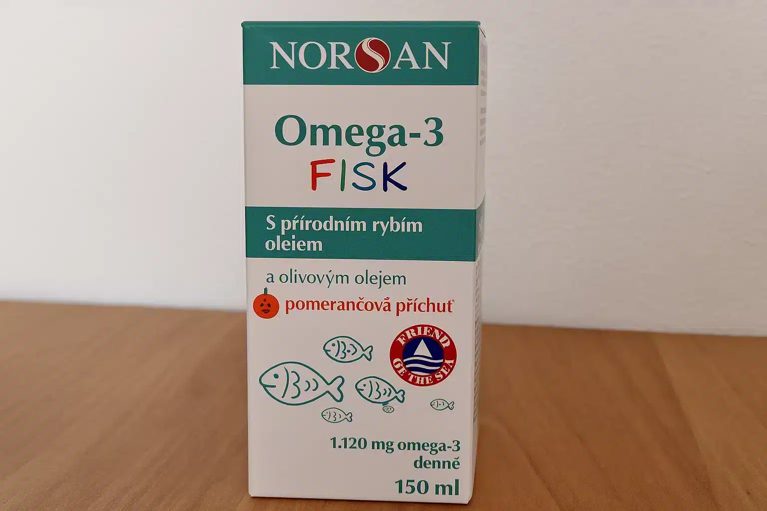 Dětský doplněk stravy NORSAN Omega-3 pro děti s pomerančovou příchutí, položený na dřevěném stole s jemným bílým pozadím, ideální pro téma Omega-3 v dětském jídelníčku.